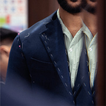 Close-up of a person wearing a navy blue blazer with pins and a light-colored shirt.