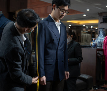 Man getting a suit measured by another man in a fitting room.