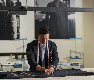 Man measuring fabric in a tailoring workshop with sewing machines in the background