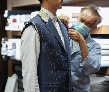 Man adjusting a suit on a mannequin in a store setting.