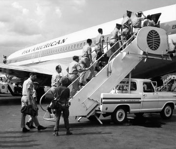 People boarding a vintage airplane with a truck nearby.
