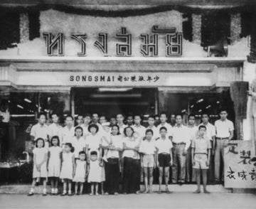 Black and white photo of a group in front of a building with text.