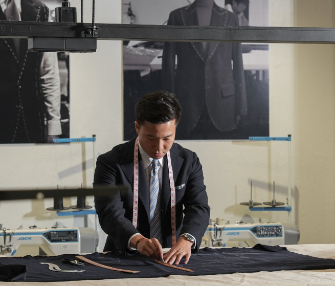 Man measuring fabric in a tailoring workshop with sewing machines in the background