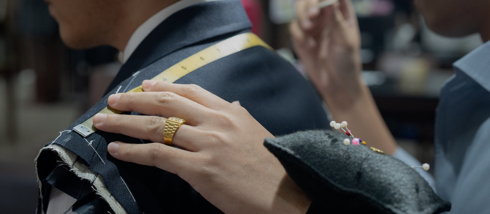 Person adjusting fabric on a garment with pins, wearing a gold ring.