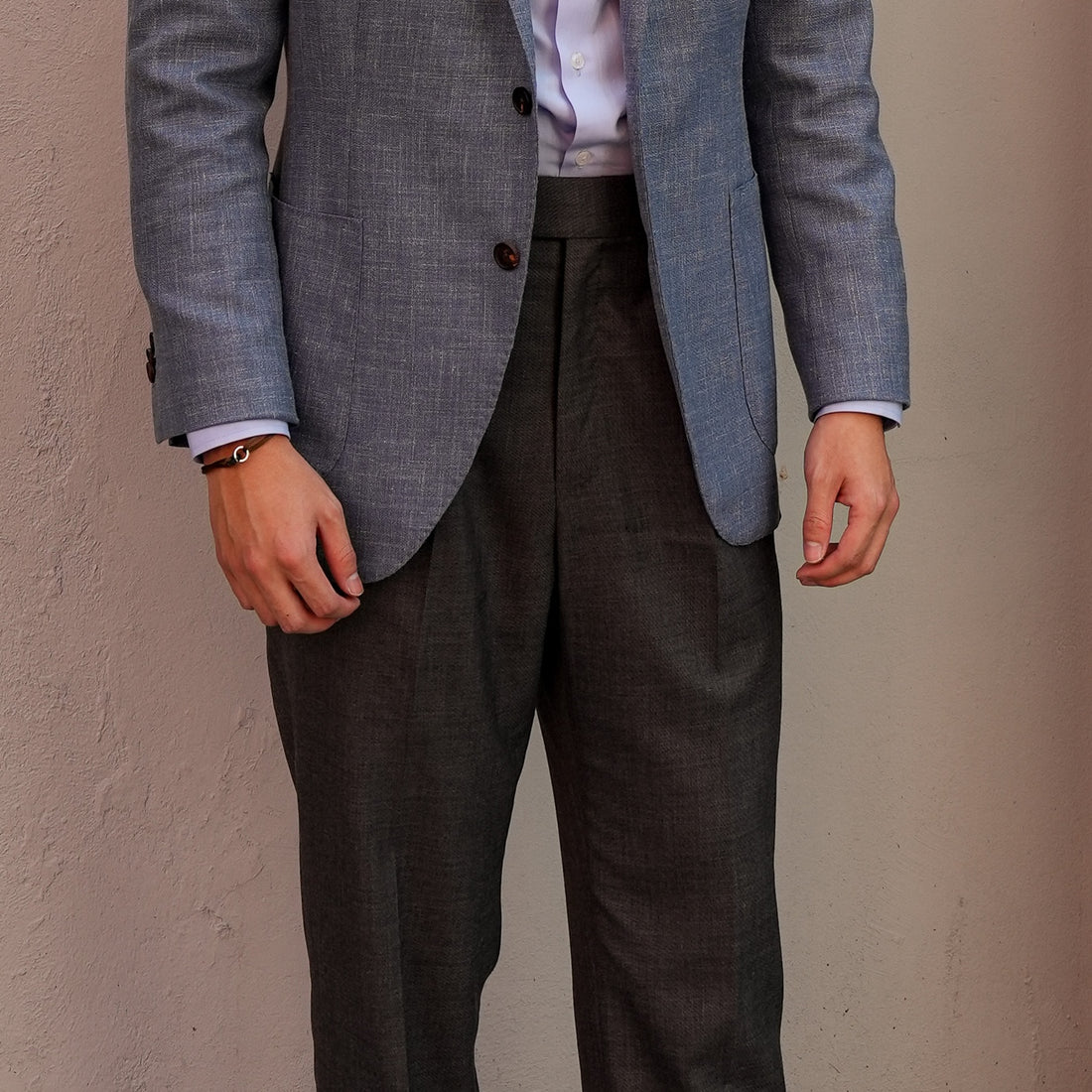Person wearing a gray blazer and dark pants against a beige wall