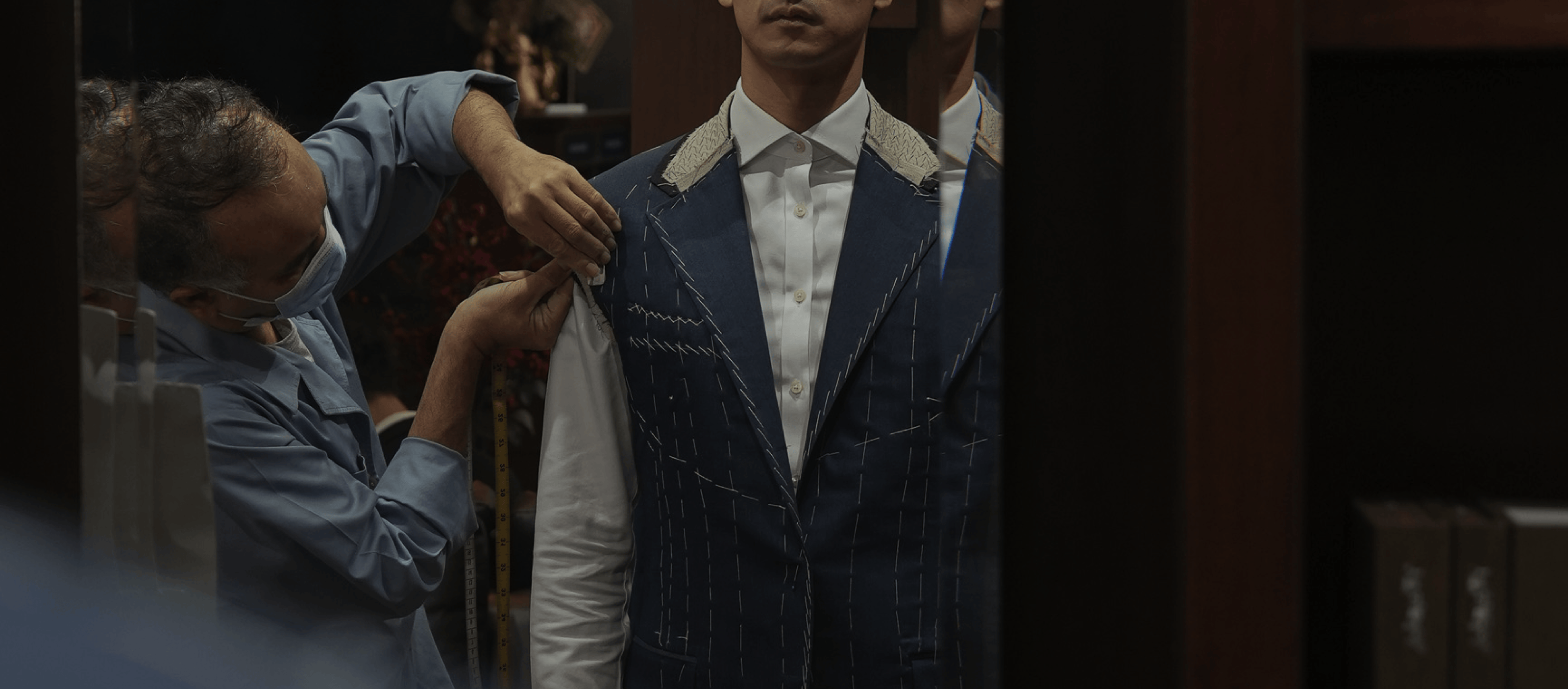 Person adjusting a suit jacket on another person in a dimly lit room.