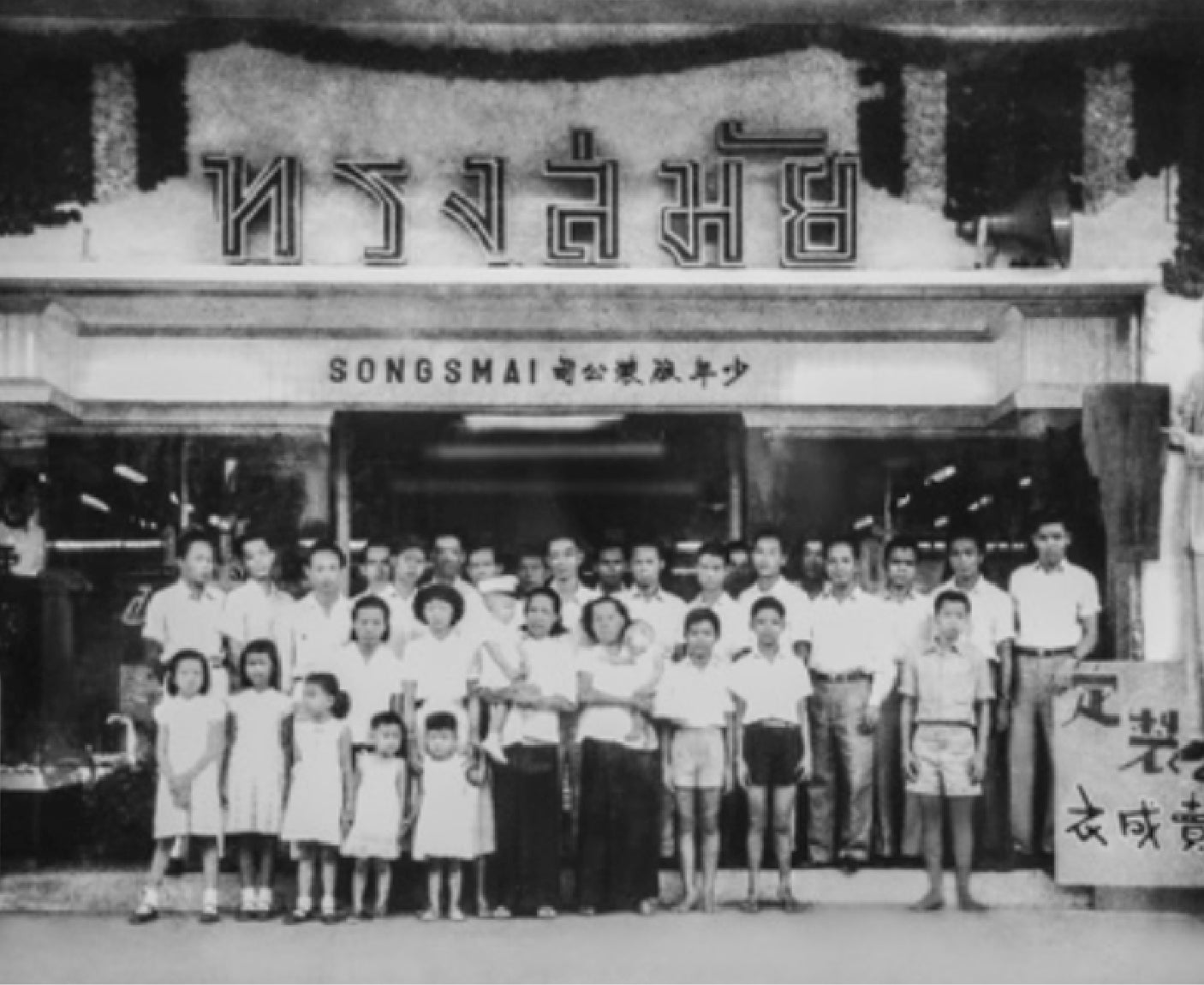 Black and white photo of a group in front of a building with text.