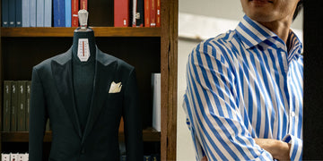 Mannequin wearing a dark suit with a white pocket square, next to a person wearing a blue and white striped shirt.